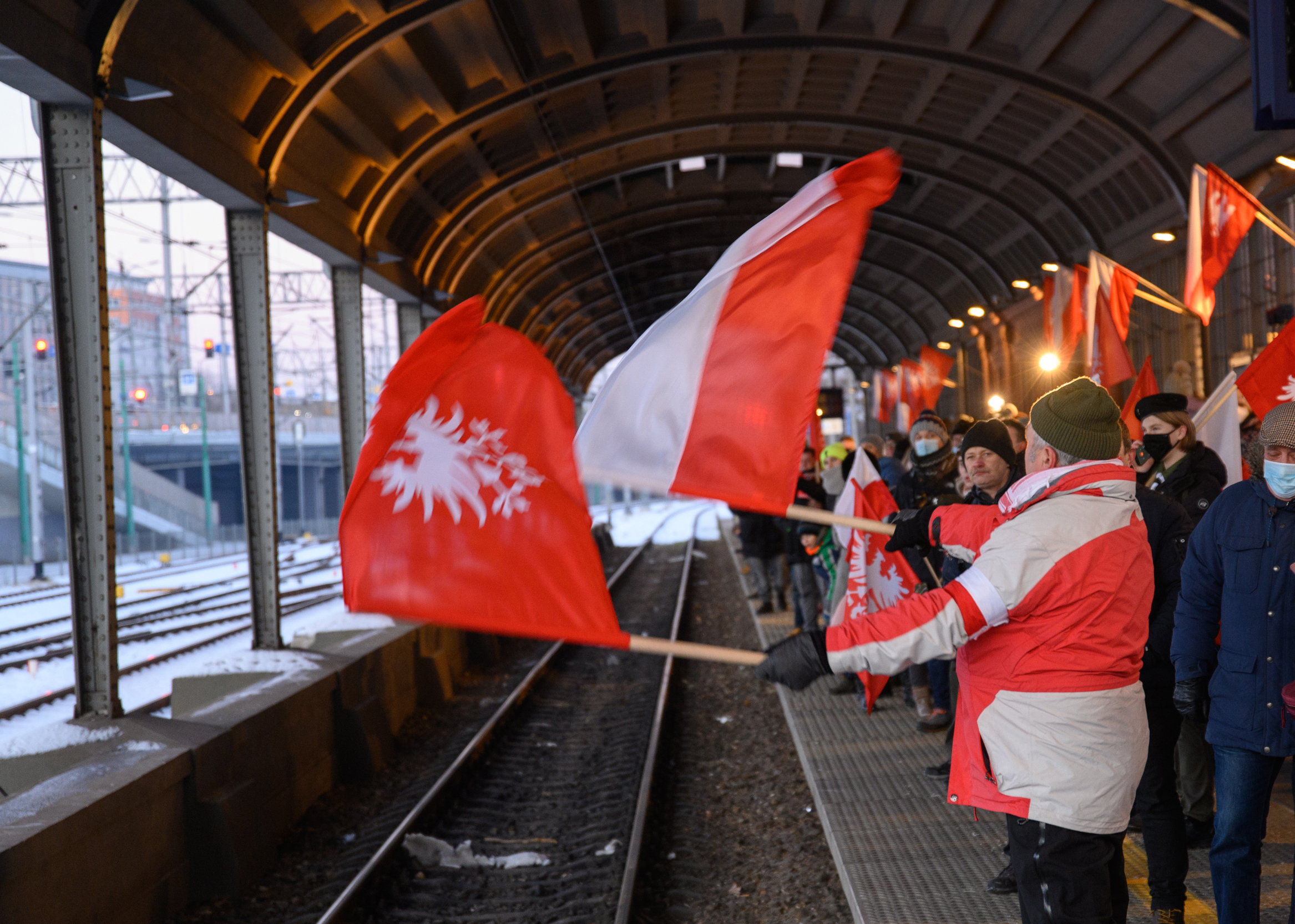 Uczestnicy wydarzenia oczekują z flagami polskimi i powstańczymi na peronie na przyjazd pociągu