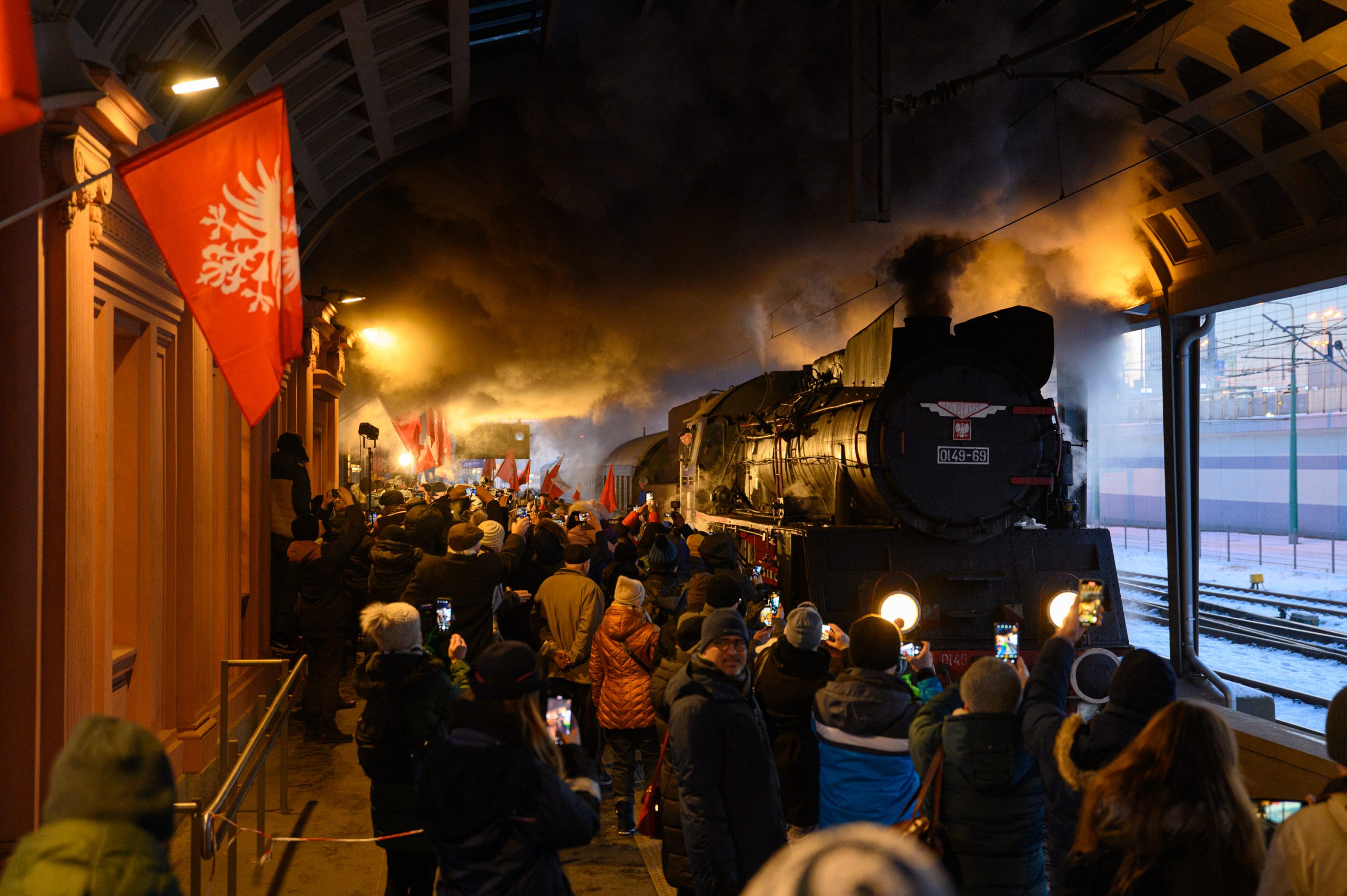 Uczestnicy wydarzenia witają wjeżdżający na peron pociąg prowadzony lokomotywą parową